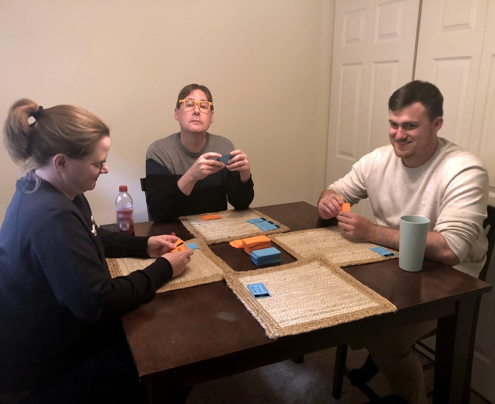 Three adults playing Expert Advice around a kitchen table, one wearing the orange Expert Eyewear