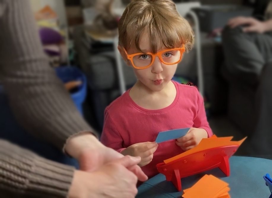 A young girl wearing the orange Expert Eyewear holds up a blue ADVICE card during a game
